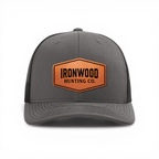 Gray cap with a brown leather patch featuring a logo and text on a white background